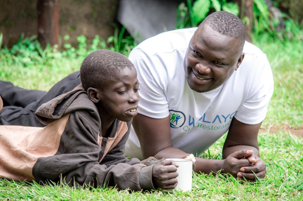 Wolayo mentor spending quiet time with a child outdoors on the grass.